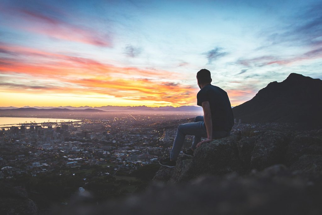 Man sitting on a ridge overlooking the city at sunset