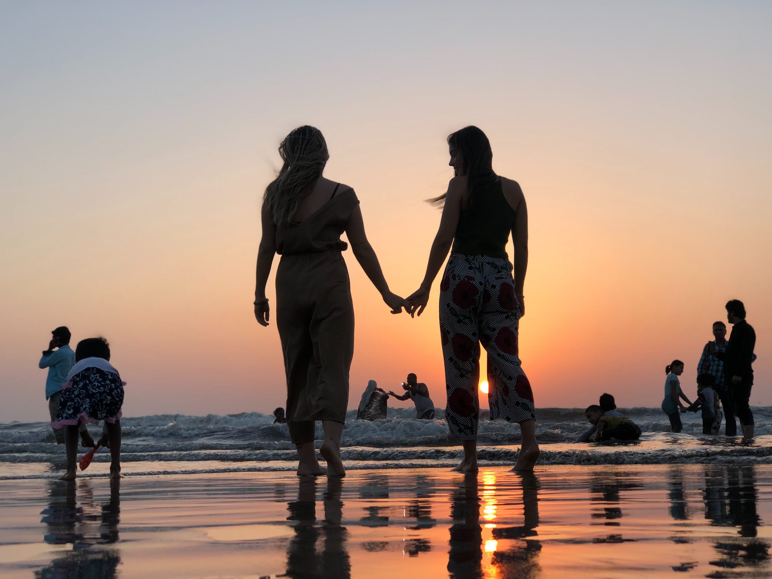 Two women holding hands in front of the sunset