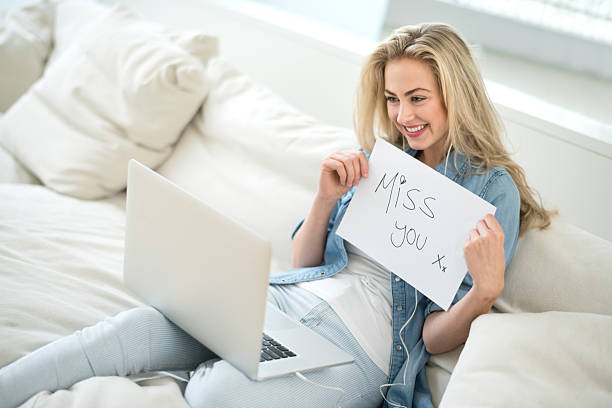 Beautiful woman video chatting with her distant boyfriend or relative and holding a "miss you" sign