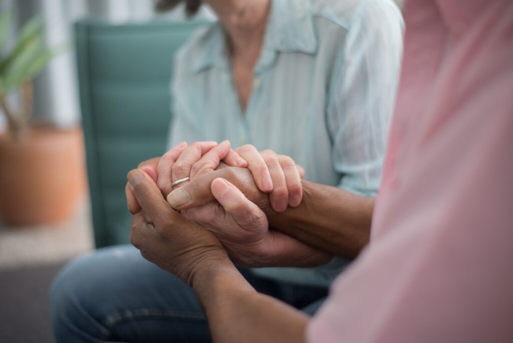 Close up of two people resting their hands together in soft light, representing emotional safety and why good relationships are good medicine.