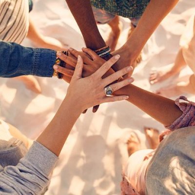 Closeup image of hands of young people with on stack. Group of mixed race friends on the beach with their hands stacked.