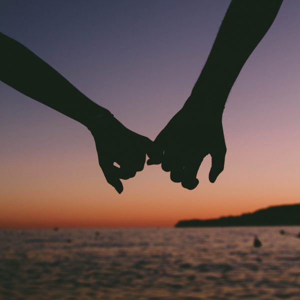 Two people linking their pinky fingers in front of a beautiful sunset